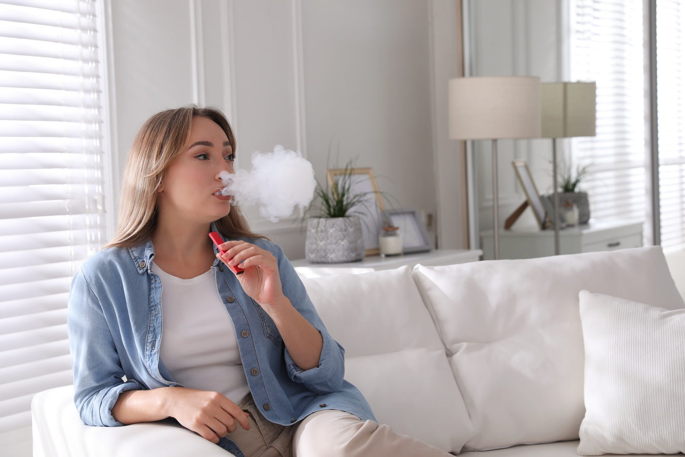 Woman sitting on couch and blowing vapour cloud into living room