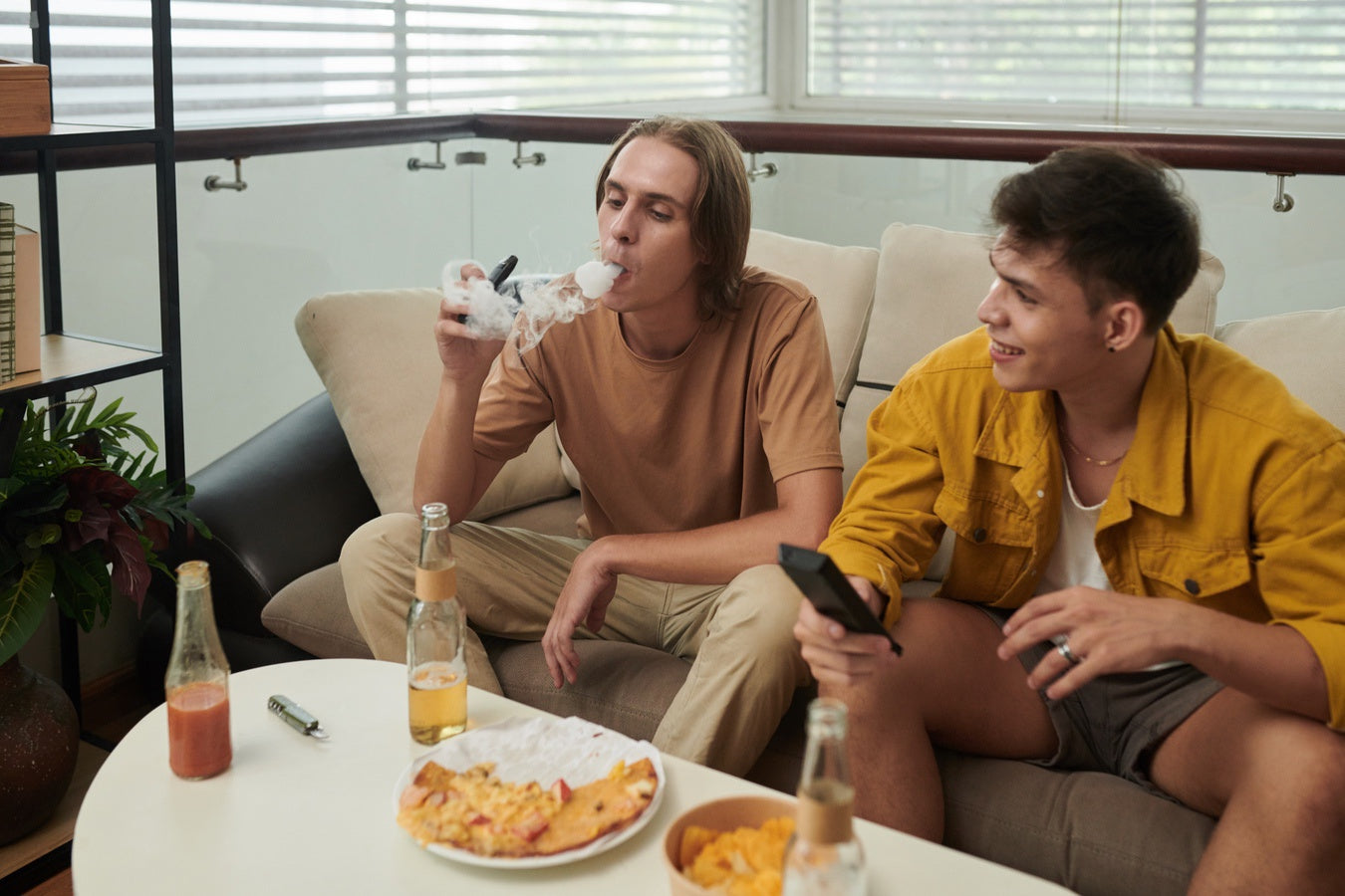 Man vaping on couch next to friend who is not vaping