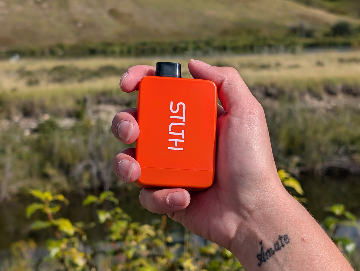 Person holding up an orange STLTH Titan Pro while going for a walk