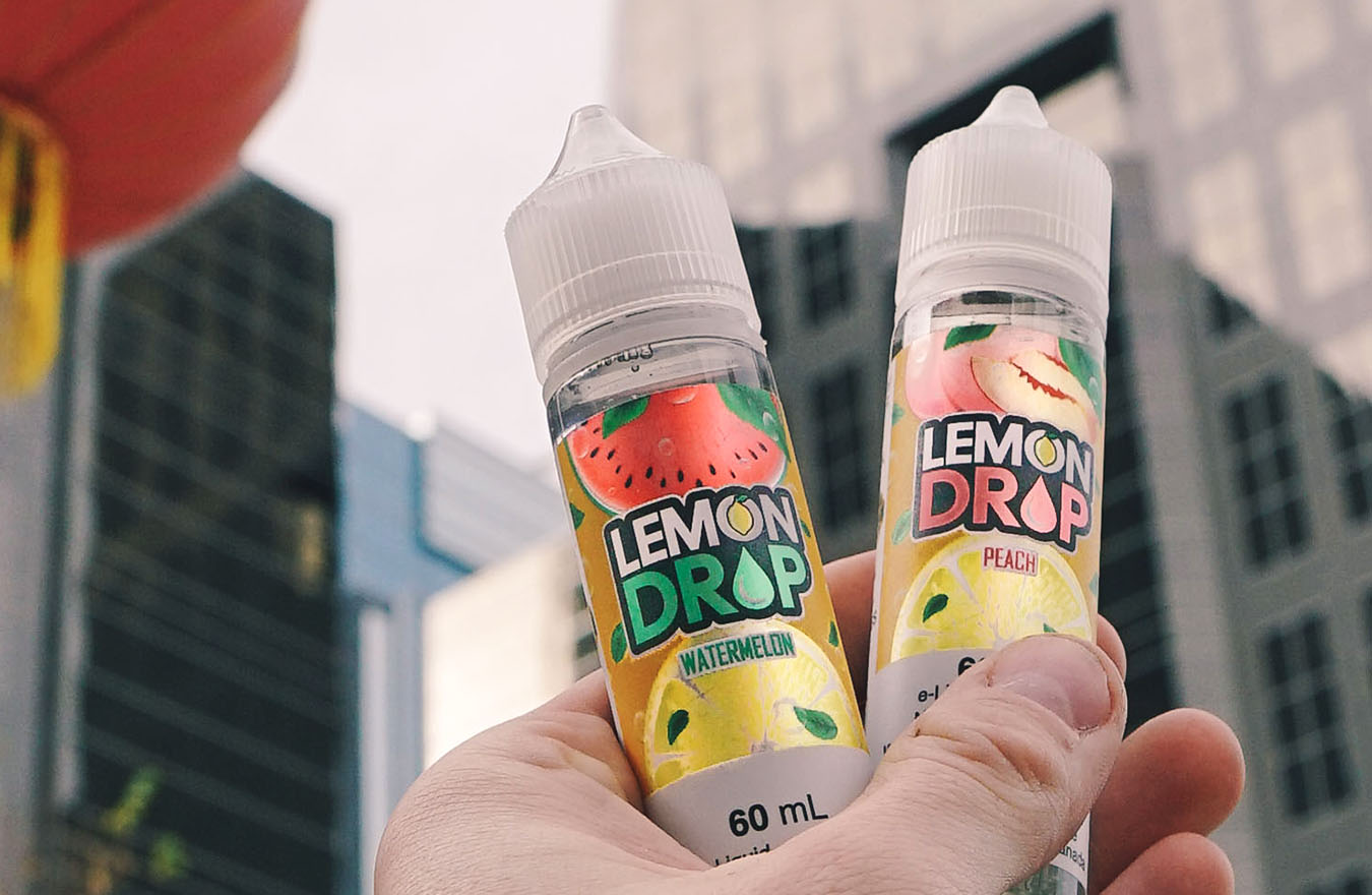 Hand holding e-liquid bottles in front of buildings
