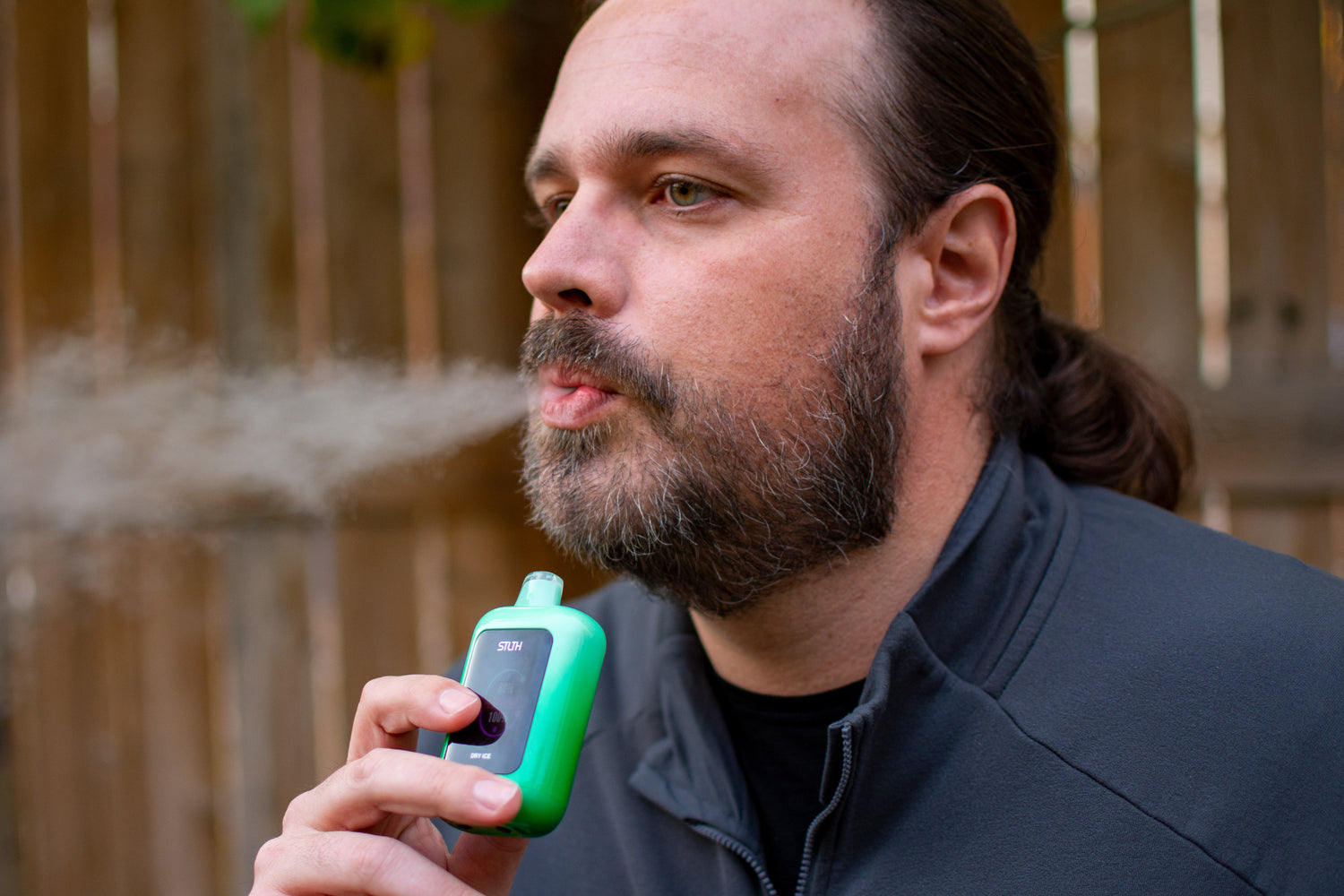 Man blowing out smoke from the green STLTH Vision vape 